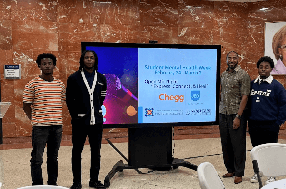 Morehouse students stand in front of a presentation screen that reads "Student Mental Health Week February 24-March 2. Open Mic Night: Express, Connect, and Heal."